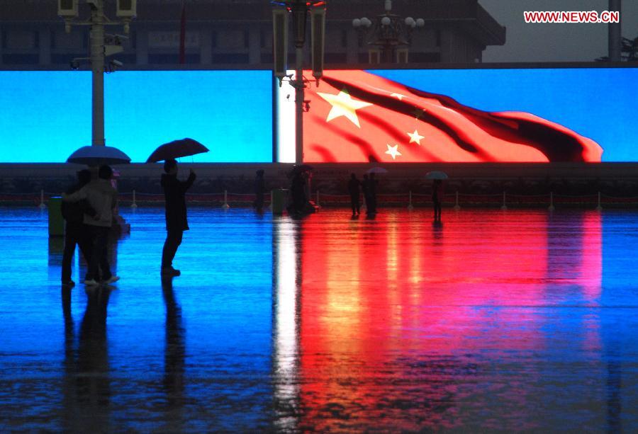 Tourists stand amid rain as they look at China's national flag shown on a large electronic board at the Tian'anmen Square in Beijing, capital of China, Nov. 10, 2012. (Xinhua/Li Gang) 
