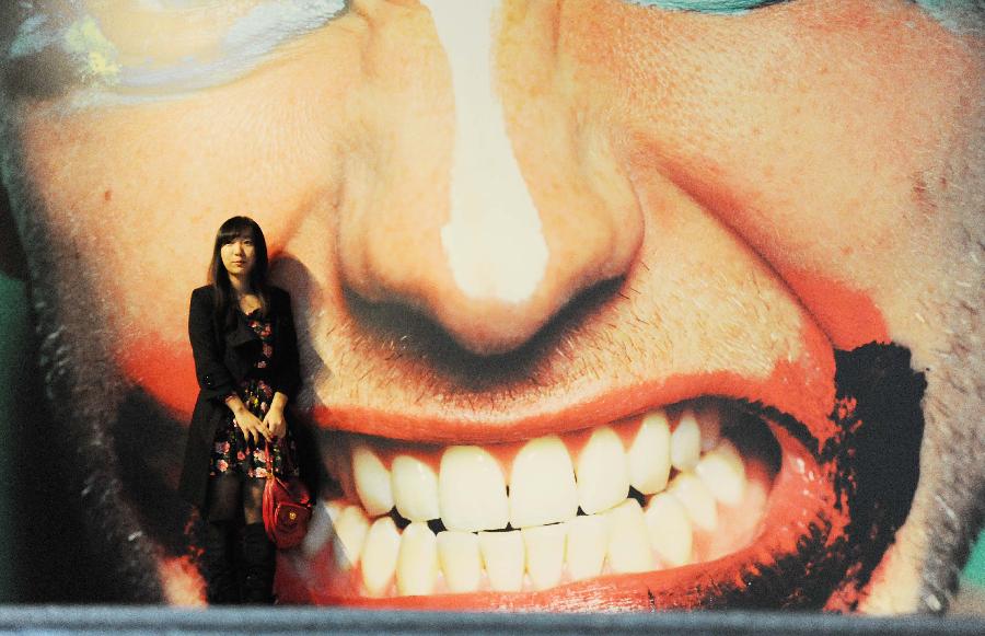 A visitor poses for a photo in front of a poster at the former site of Shanghai Art Museum in east China's Shanghai Municipality, Nov. 11, 2012. (Xinhua/Lai Xinlin) 