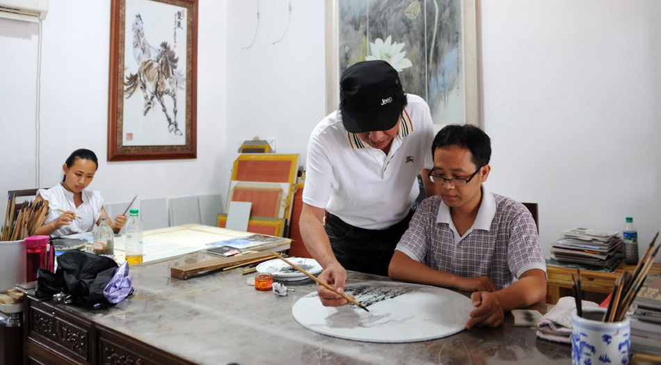 Li Bin (C) instructs a student to draw on a porcelain plate at a workroom in Jingdezhen, east China's Jiangxi Province, Aug. 18, 2012. (Xinhua/Zhang Ruiqi)