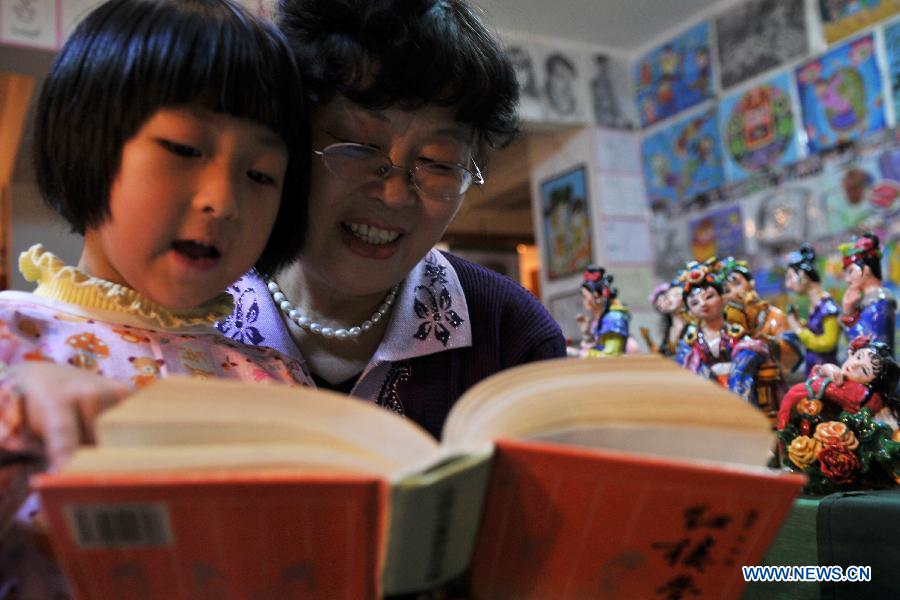 Li Lingxiu tells the storis of "A Dream of the Red Chamber" to a girl in Lanzhou, capital of northwest China's Gansu Province, Nov. 20, 2012. The retired worker Li Lingxiu created 30 clay sculptures of characters in the ancient Chinese novel classic "A Dream of the Red Chamber". (Xinhua/Chen Bin) 