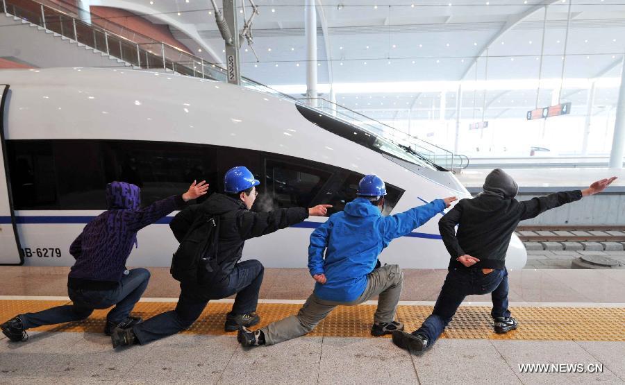 Passengers imitate the hand signals of flight deck crew of aircraft carrier beside a high-speed train at the Harbin West Railway Station in Harbin, capital of northeast China's Heilongjiang Province, Dec. 1, 2012. The world's first high-speed railway in areas with extremely low temperature, which runs through three provinces in northeastern China, started operation on Saturday. The railway links Harbin, capital of Heilongjiang Province, and Dalian, a port city in Liaoning Province. (Xinhua/Wang Jianwei)