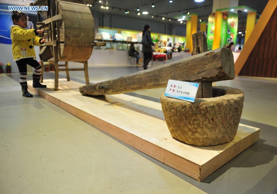 A young girl tries to operate a farm tool during an exhibition on farming culture of Zhuang ethnic group in Nanning, capital of southwest China's Guangxi Zhuang Autonomous Region, Dec. 1, 2012. (Xinhua/Huang Xiaobang)