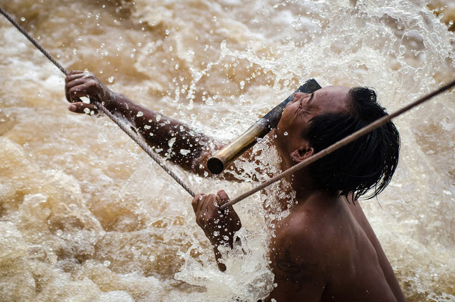“Fisherman in the waterfall”：A fisherman risks his life when fishing in the Mekong River on Si Phan Don Island. It is said that the fisherman must hold on tight to the rope with all his attention, so other things can only be put in the mouth, including the knife.(Photo/Xinhua)