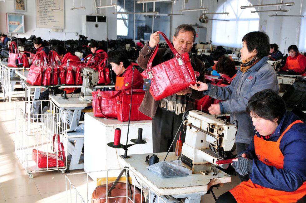 Kim Byungcho (L standing) inspects at a plant of his leather product company in Rushan, east China's Shandong Province, Feb. 2, 2012.(Xinhua Photo) 