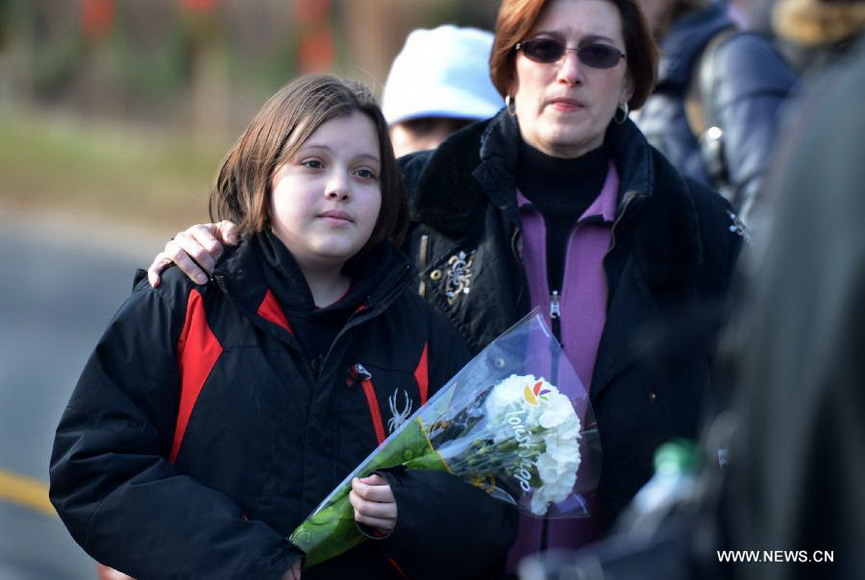 A girls at the company of her mother presents flowers near Sandy Hook Elementary School, where a gunman opened fire on school children and staff in Newtown, Connecticut, Dec. 15, 2012. A shooting incident on Friday morning in the elementary school in Newtown of the Connecticut State of the United States killed at least 28 people, including 20 children. (Xinhua/Wang Lei)