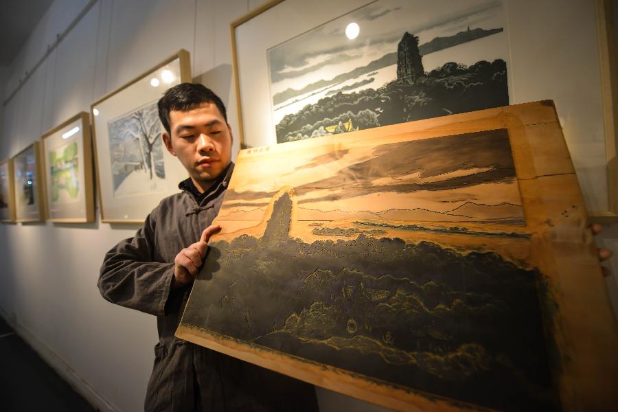 A staff member shows a woodblock painting work during an exhibition of woodblock paintings depicting the scenery of the West Lake in Hangzhou, capital of east China's Zhejiang Province, Dec. 18, 2012. The technique of woodblock printing was listed as a state intangbile cultural heritage of China in 2008. (Xinhua/Xu Yu) 