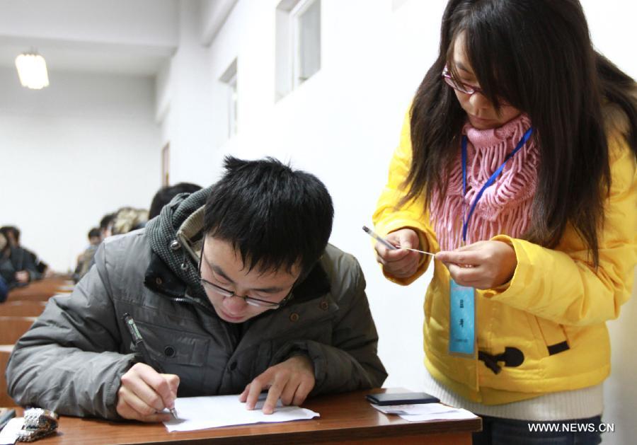 An invigilator checks identity certificate of a candidate before National College English Test at Jiangsu University in Zhenjiang, east China's Jiangsu Province, Dec. 22, 2012.