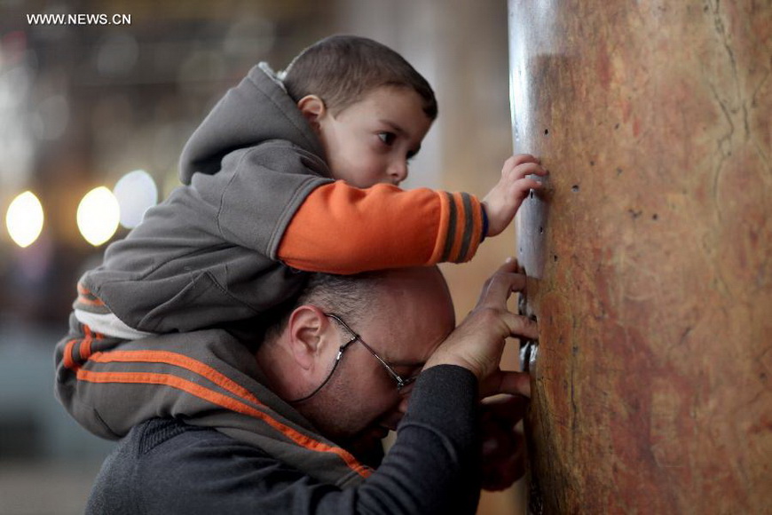 A worshiper and his son touchs a column inside the Church of the Nativity, traditionally believed to be the birthplace of Jesus Christ, as they attend the Christmas celebrations in the West Bank biblical town of Bethlehem on Dec. 24, 2012. (Xinhua/Fadi Arouri)