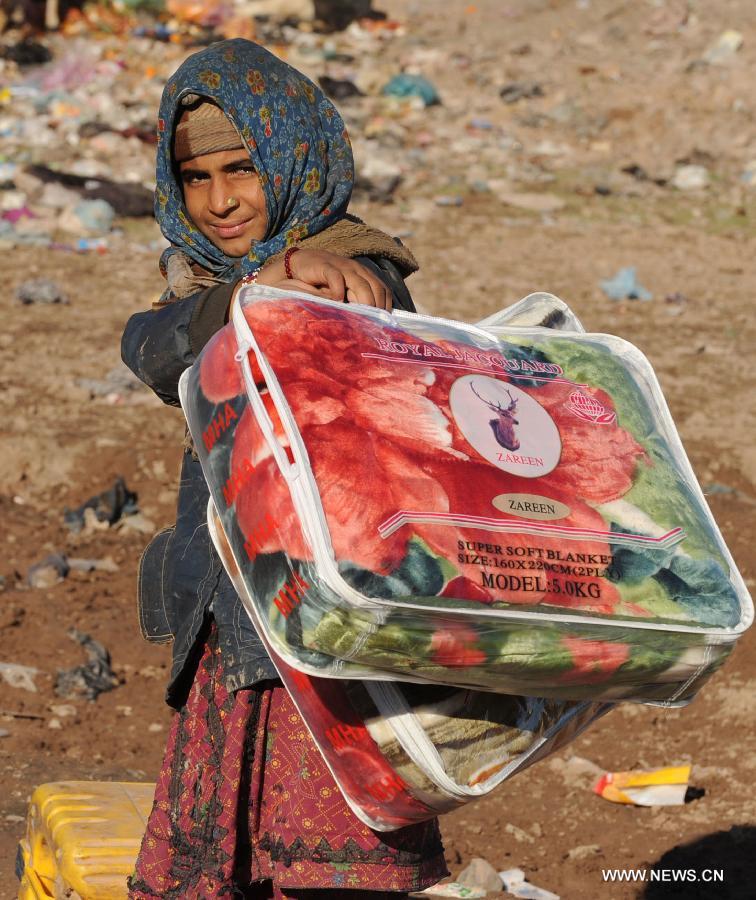 An Afghan poor girl carries blankets donated by rich people in Herat province of western Afghanistan on Jan. 5, 2013. Hundreds of poor families received winter relief assistance on Saturday. (Xinhua/Sardar)
