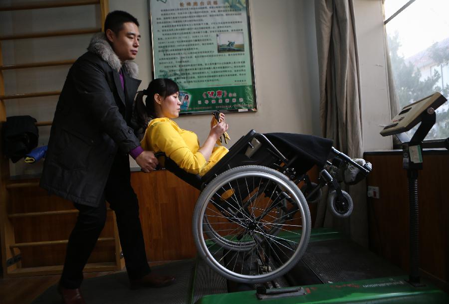Zhang Lili, a teacher who lost her legs while saving two students from an onrushing bus, gets her wheel chair down the treadmill under the help of her husband Li Ziye at the China Rehabilitation Research Center in Beijing, capital of China, Jan. 7, 2013. Zhang, who successfully pushed the students out of the harm's way but unable to avoid the bus herself and lost her legs in the accident, has been receiving rehabilitative treatment here for over 4 months. Zhang makes great efforts now in order to be able to walk again. (Xinhua/Jin Liwang) 