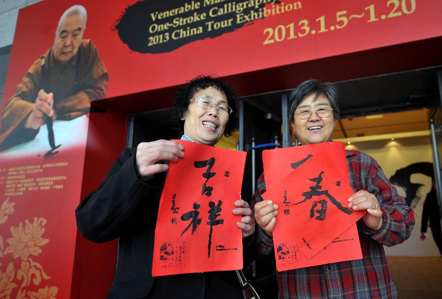 Two visitors pose for a photo with the calligraphy rubbings at a tour exhibition of Venerable Master Hsing Yun's One-Stroke Calligraphy held at the Hainan Provincial Museum in Haikou, capital of south China's Hainan Province, Jan. 8, 2013. A total of 55 calligraphy works by master Hsing Yun were on display at the exhibition that will last until Jan. 20. (Xinhua/Guo Cheng) 