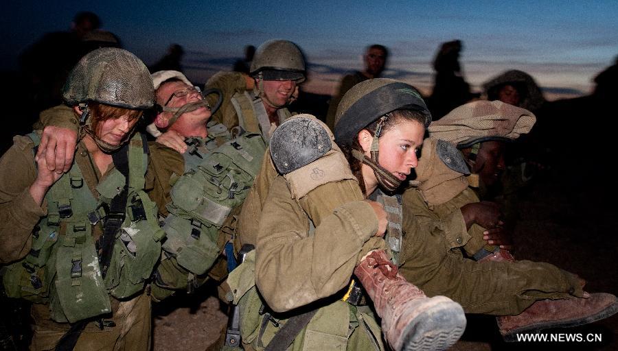 Israeli woman soldiers carry an "injured" soldier with male soldiers during a military drill at the western part of Sede Boqer, southern Isreal, on Dec. 13, 2012. (Xinhua/Yin Dongxun)