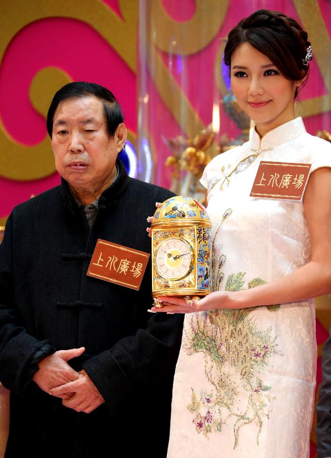 Artist Zhang Tonglu (L) looks on as a cloisonne clock he made is presented by Elva Ni, the winner of 2005 Miss Chinese Toronto Pageant, during an exhibition in south China's Hong Kong, Jan. 22, 2013. An exhibition of Zhang Tonglu's cloisonne art works was held here on Tuesday, showing 22 pieces of cloisonne works. (Xinhua/Li Peng) 