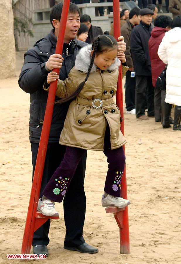 File photo taken on Jan. 17, 2009 shows a little girl learns walking on stilts with the help from a family member at a temple fair in Zhengzhou, capital of central China's Henan Province. Temple fair in central China area is an important social activity for local people. The ancient temple fairs in central China were ceremonious sacrificial rituals. As time goes by, the focus of temple fair activities has shifted from "gods" to "people". The modern temple fair in central China is a platform of displaying folk culture as well as a channel for commodity circulation. According to statistics from the provincial cultural sector, there are about 35,000 temple fairs each year in Henan. (Xinhua/Wang Song)
