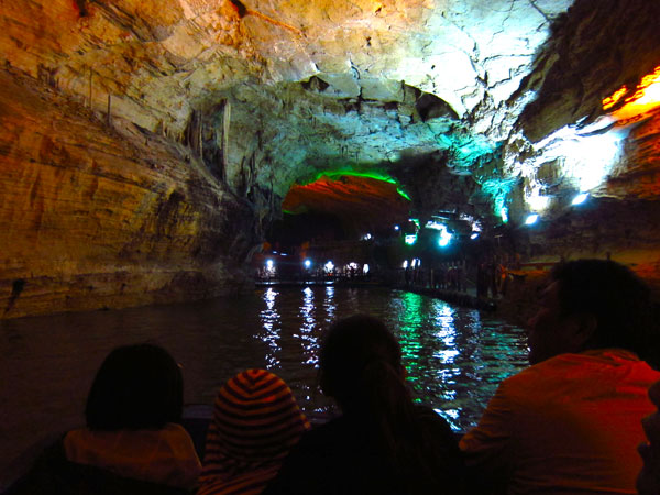 Visitors gaze at the surrounding caves while cruising along Yellow Dragon Cave's Rattle River. (Photo/CRI)