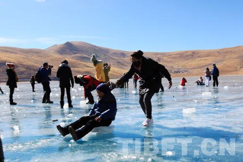 Toursits play on the ice surface of the Yamzhog Yumco Lake on Feb.14, 2013. [Photo/China Tibet Online]