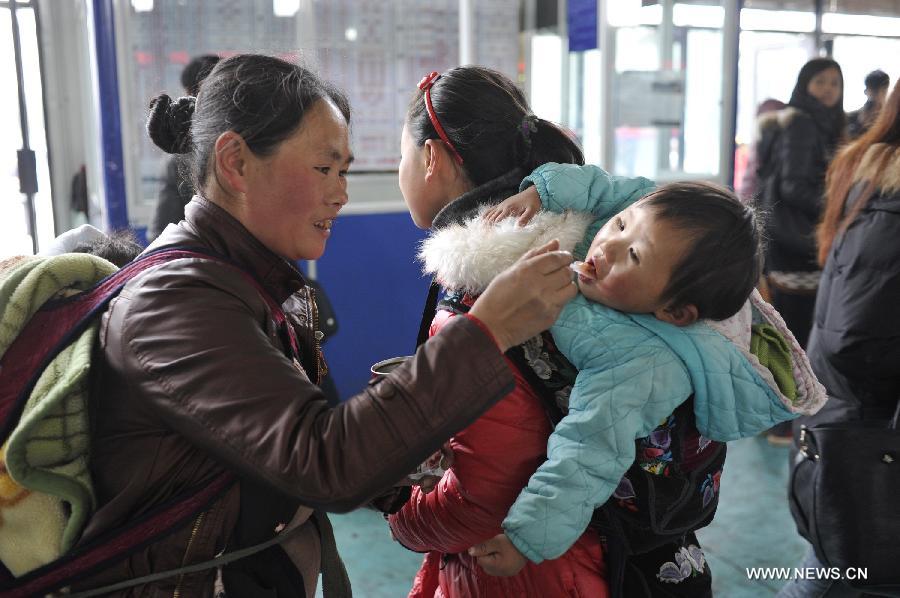 A woman feeds a child canned mixed porridge while waiting for their bus at Jinyang bus station in Guiyang, capital of southwest China's Guizhou Province, Feb. 17, 2013. Migrant workers, together with their children, started to return to the urban areas to work after the one-week Spring Festival holiday ended. (Xinhua/Ou Dongqu)