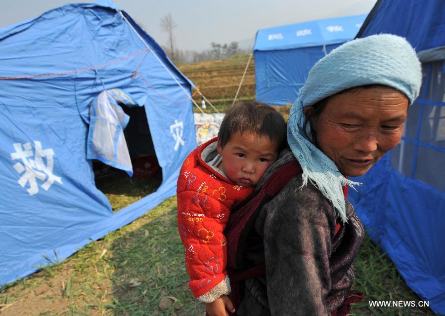 A woman with a child stand in front of a relief tent at Qiandian Village of Liantie Township in Eryuan County of Dali Bai Autonomous Prefecture, southwest China's Yunnan Province, March 4, 2013. A 5.5-magnitude earthquake hit Eryuan County on March 3. Thirty people have been confirmed injured, while some 21,000 people have been evacuated. (Xinhua/Lin Yiguang) 