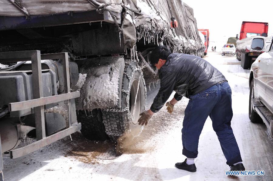 A driver sprinkles salt on the tyres bound with skidproof chains as vehicles queue to pass the segment of state highway 109 which is covered with snow near Nalong Village in Damxung County, southwest China's Tibet Autonomous Region, March 18, 2013. A snowstorm here made an icy road on the segement of state highway 109 near Nalong Village, causing many vehicles truck on the road. (Xinhua/Liu Kun)