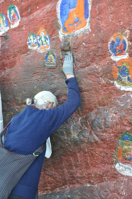Photo shows a praying Buddhist believer, who touches the Six-Syllable Mantra Prayer engraved on the Yaowang Mountain stones on the Thousand-Buddha Cliff. [Photo/Xinhua]