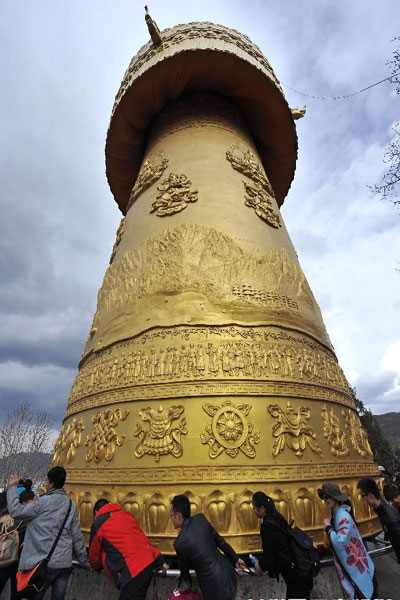 Some tourists are pushing forward the huge prayer wheel in the "Dukezong" Ancient Town. [Photo/Xinhua] 