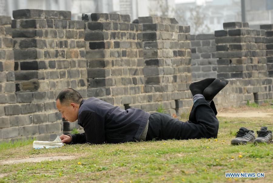 A tourist reads a book on the lawn on the old city wall in Xiangyang, central China's Hubei Province, March 21, 2013.(Xinhua/Li Xiaoguo)