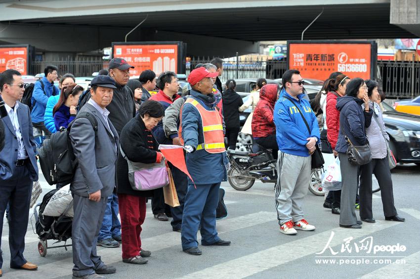With the instruction of a traffic warden, pedestrians cross the road in an orderly manner at a crossing of Da Wang Road on April 9,2013.(People's Daily Online/Weng Qiyu)