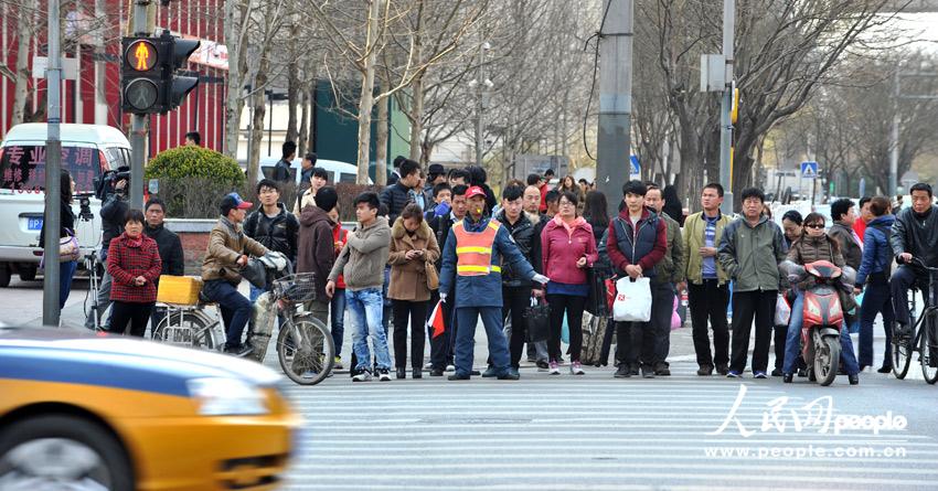 With the instruction of a traffic warden, pedestrians cross the road in an orderly manner at a crossing of Da Wang Road on April 9,2013.(People's Daily Online/Weng Qiyu)