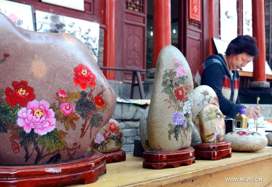 A painter sells peony artwares at a temple fair in Luoyang, central China's Henan Province, April 11, 2013. Known as the "city of peony", Luoyang has created an industry chain on peony in recent years. Various crafts and products of peony have been developed to serve the local economy. (Xinhua/Wang Song)