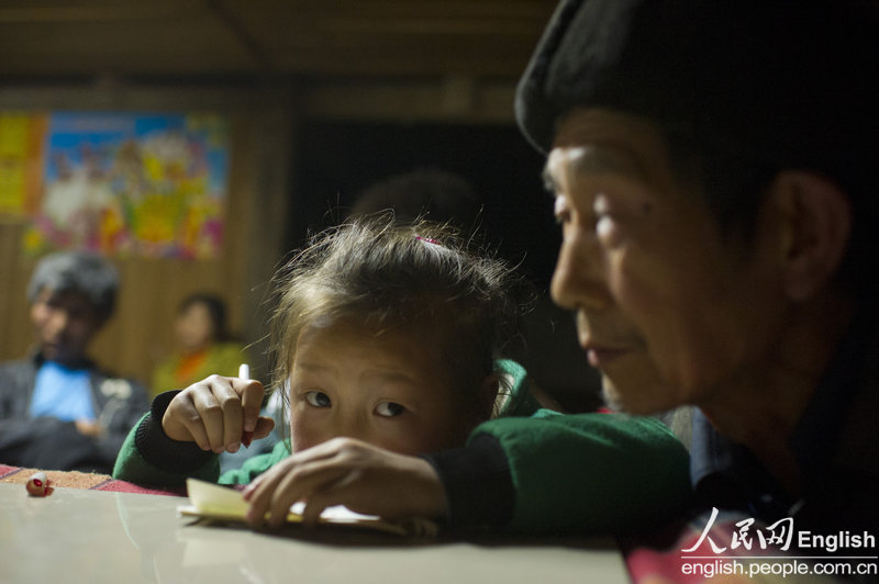 Yu Qiyun's sister does her homework with the help of her grandfather at home, Sangzhi county, Hunan province April 11, 2013.  (Photo/ People's Daily Online)