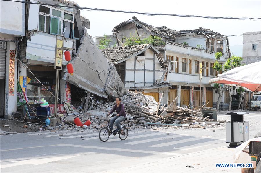A local resident rides in front of collapsed houses in quake-hit Lushan County, Ya'an City, southwest China's Sichuan Province, April 20, 2013. (Xinhua/Jin Xiaoming)