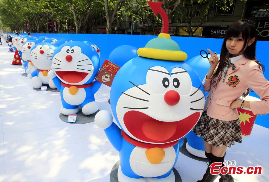A member of the Chinese girl singing group SNH48 poses with Doraemon, a robot cat in a Japanese animation series, at Xintiandi in Shanghai, April 26, 2013. An exhibition featuring 100 Doraemons with 100 different gadgets and machines it used in the series is being held at Xintiandi until June 16. It is the largest exhibition featuring Doraemon on the Chinese mainland. (CNS/Pan Suofei)