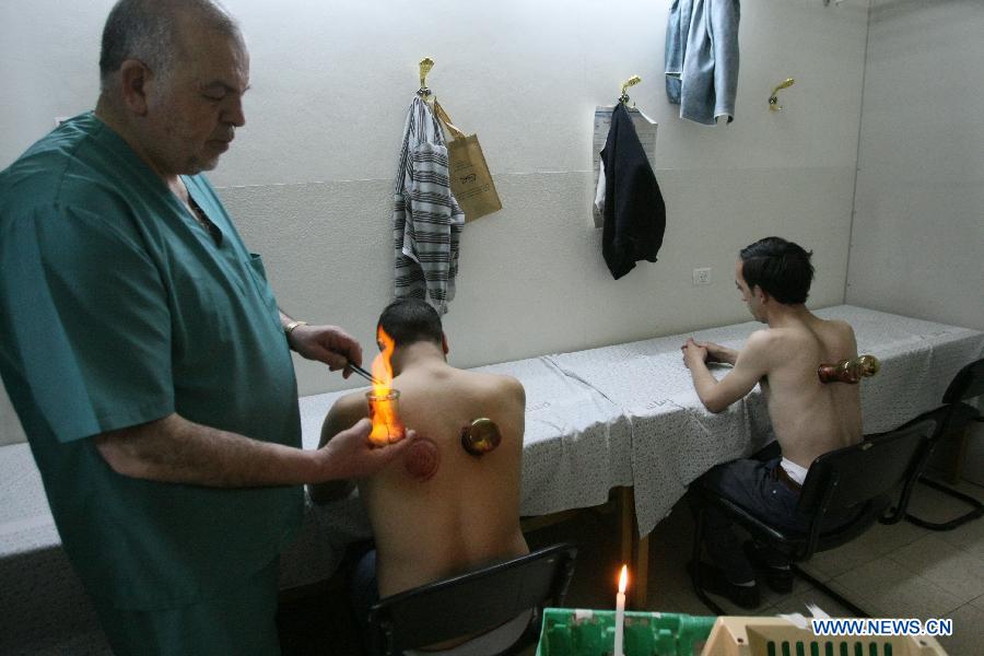 Palestinian practitioner puts a cup on a patient's back during a blood cupping session in the West Bank city of Hebron, on May 2, 2013. In the West Bank city of Hebron Cupping therapy is used to treat many medical conditions like skin problems, blood disorders, fertility disorders and stroke. The process involves pricking the skin with needles before immediately applying a cup on top to draw congealed blood. (Xinhua/Mamoun Wazwaz)