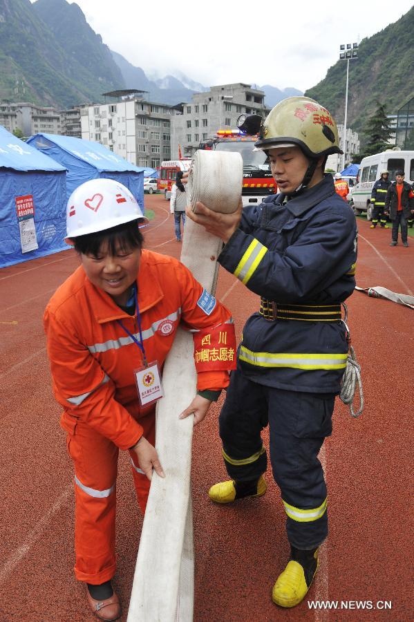 A volunteer (L) helps a fire fighter roll a water hose after a fire fighting drill held in a school playground in the quake-hit Baoxing County, southwest China's Sichuan Province, May 2, 2013. The school playground was served as the largest evacuation settlement for nearly 4,000 displaced people in Baoxing after the strong earthquake occurred in last month. (Xinhua/Lu Peng)