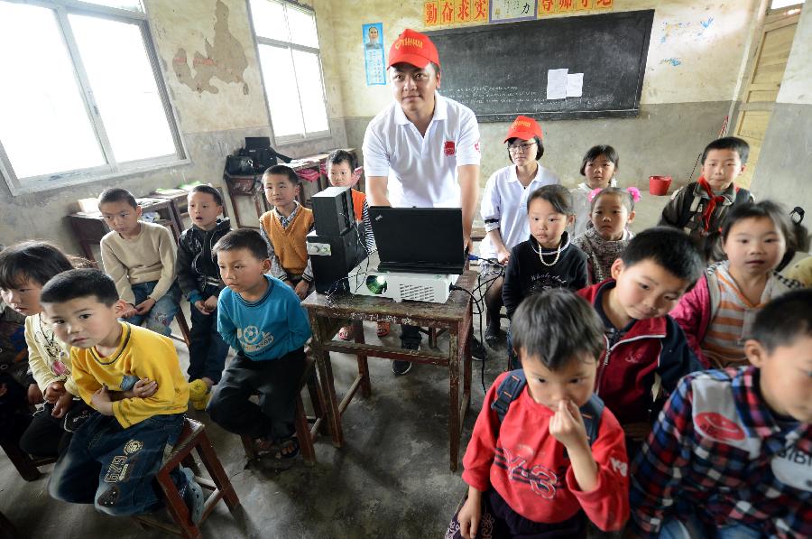 Xiong Hailong (C), a college student serving as village official, shows film for pupils of the Shahu Elementary School at a temporarily-erected "cinema" in Jingkou Township of Nanchang County, east China's Jiangxi Province, May 2, 2013. Volunteers in Jingkou Township organized a film projection team and projected films in 23 elementary and middle schools for students, most of whom had never seen a movie before. (Xinhua/Zhou Ke)
