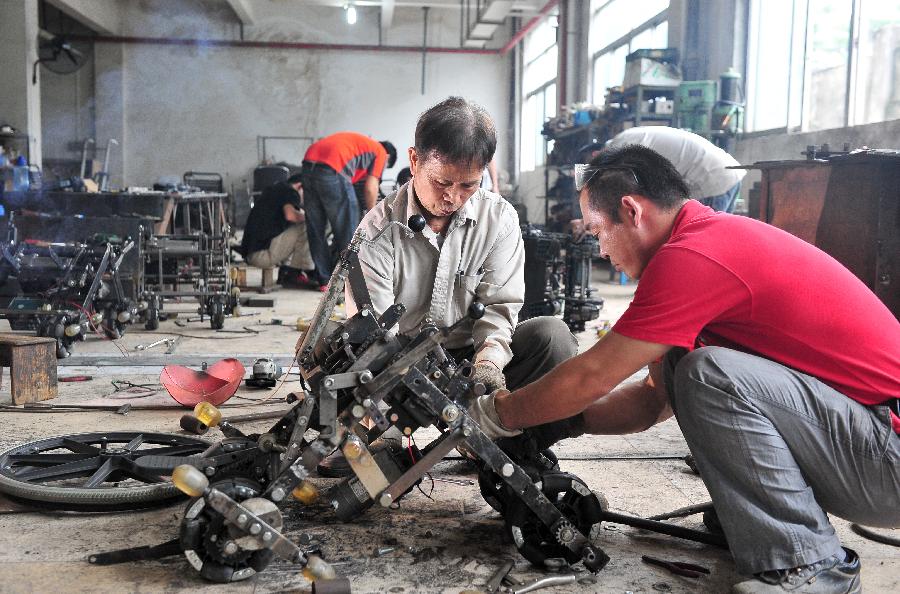 Liu Tie'er (L Front) installs a wheelchair he invented in a workshop in Guangzhou, capital of south China's Guangdong Province, May 6, 2013. Liu Tie'er, a 71-year-old local resident, invented a wheelchair capable of climbing stairs in an effort to help his disabled wife and many more who are in need. (Xinhua/Lu Hanxin) 