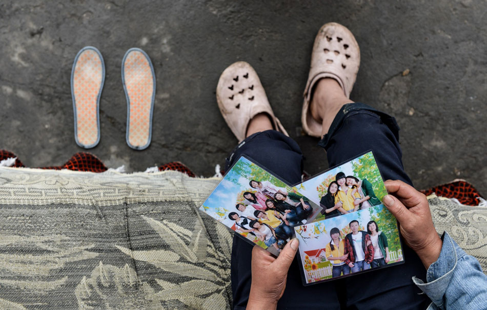 Zhao Siqiong looks at the photos of her daughter with classmates in Lushan, Sichuan province on May 10, 2013. A pair of hand-embroidered insoles made by her daughter was placed next to her. Her daughter died in the Lushan Earthquake on April 20, 2013. Zhao's husband burned all the items of their daughter at the funeral for fear that they would sadden Zhao. The only memory left to Zhao is the pair of hand-embroidered insoles. (Xinhua/Bai Yu)