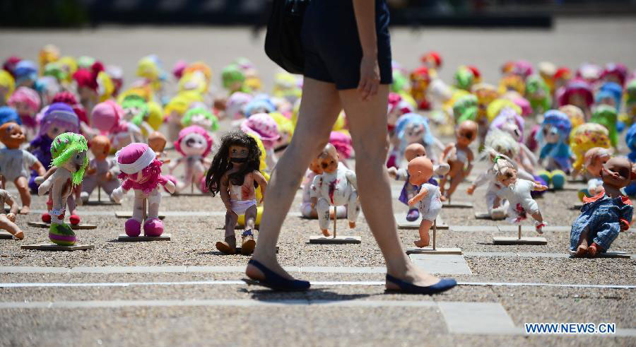 A woman walks past "abused" dolls at Rabin Square in Tel Aviv, Israel, on May 23, 2013. Approximately 1,000 dolls, made as if they have been abused, were on a display here to arouse public awareness of child abuse and its long-term effect on those victims. (Xinhua/Yin Dongxun) 