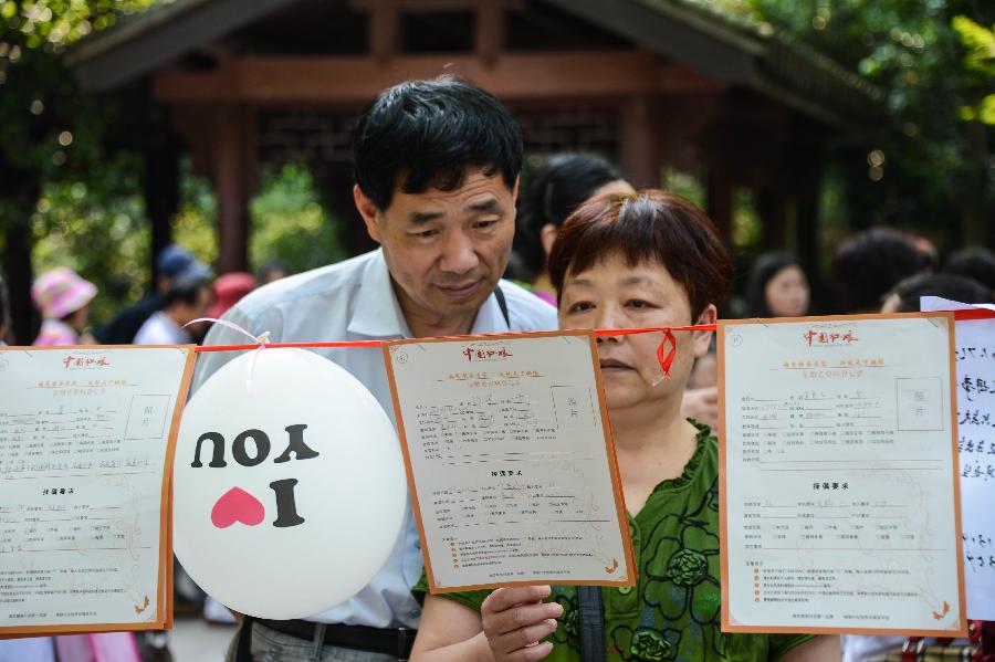 People view marriage-seeking leaflets during a blind date event at Huanglongdong scenic area in Hangzhou, capital of east China's Zhejiang Province, May 25, 2013. The event attracted over 5,000 participants, including both young singles and their parents. (Xinhua/Xu Yu)