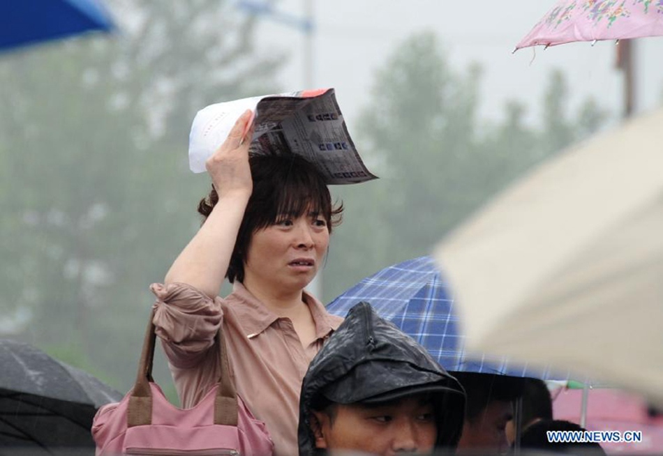 A mother waits in rain for her kid taking the national college entrance exam in Gu'an, north China's Hebei Province, June 7, 2013. Some 9.12 million applicants are expected to sit this year's college entrance exam.
