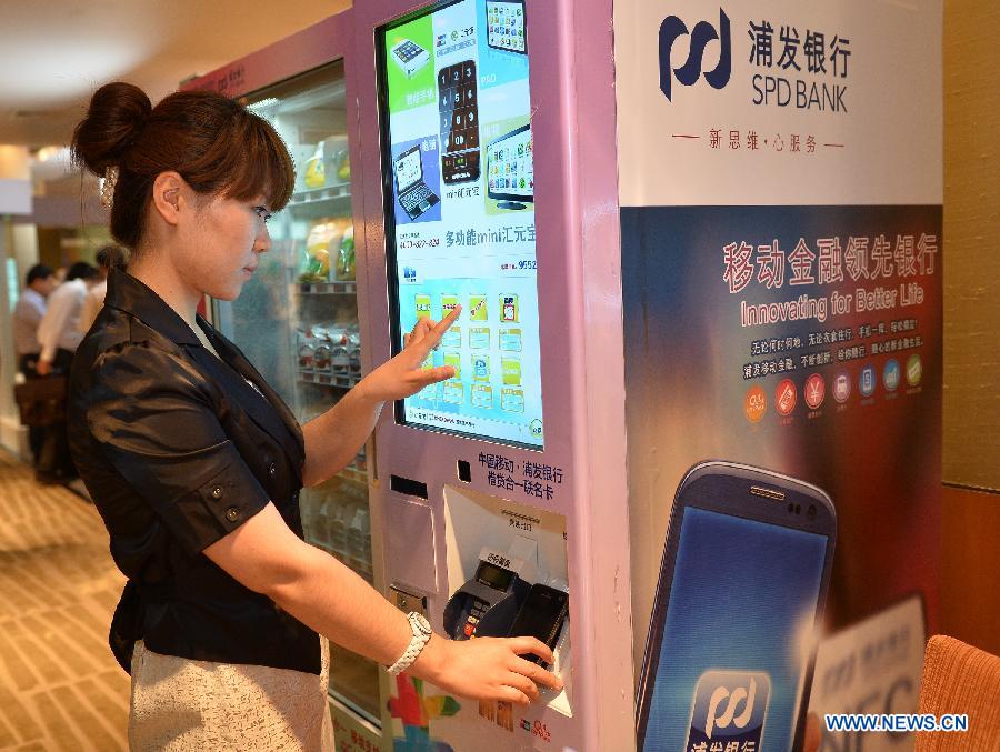 A staff member shows how to use a mobile phone with mobile payment platform to pay for the shopping through a vending machine in Beijing, capital of China, June 9, 2013. China's UnionPay bank card network established the mobile payment platform with telecom operator China Mobile, according to a press conference on Sunday. (Xinhua/Li Xin)