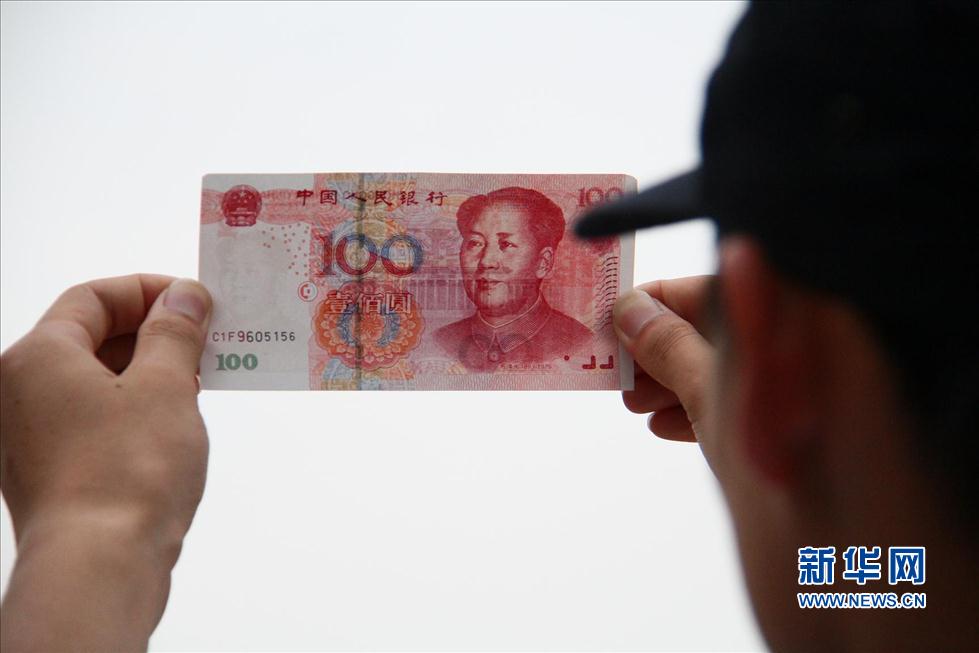 A man holds up a 100-yuan fake note bearing the serial number ‘C1F9.’ (Photo/Xinhua)