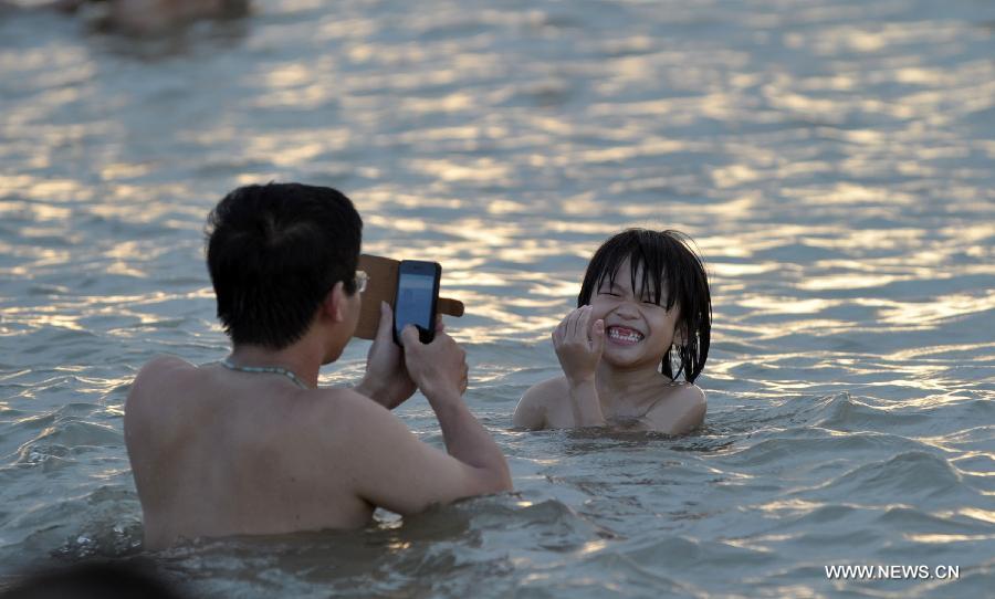 A man take photos of a child in the sea near Haikou, capital of south China's Hainan Province, June 29, 2013. The highest temperature in Haikou reached 35 degree centigrade, driving local residents to the seashore. (Xinhua/Zhao Yingquan)