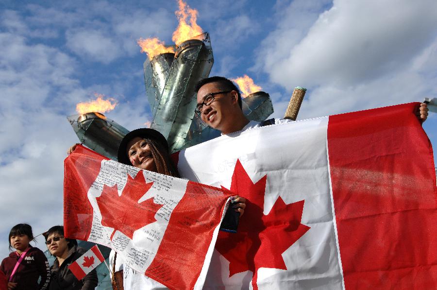 A couple holding Canadian national flags poses for a photo with the lit Winter Olympics cauldron as the background during the Canada Day celebrations in Vancouver, Canada, on July 1, 2013. Tens of thousands of spectators flooded the streets of Vancouver to participate in Canada Day festivities. (Xinhua/Sergei Bachlakov)