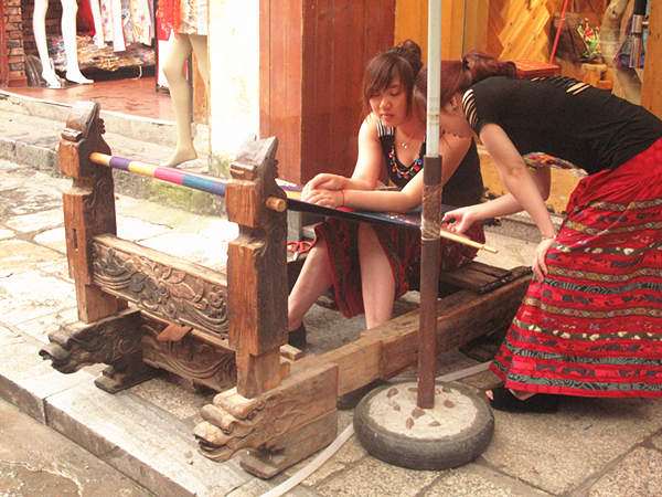 Two girls display how to weave local cotton cloth. With a history of over 1,400 years, West Street is located in the center of Yangshuo County and is also called Foreigner's Street. Here, the bars, hotels, Internet cafes and painting shops’ decoration style is mostly Chinese mixed with Western culture. (CnDG by Jiao Meng)