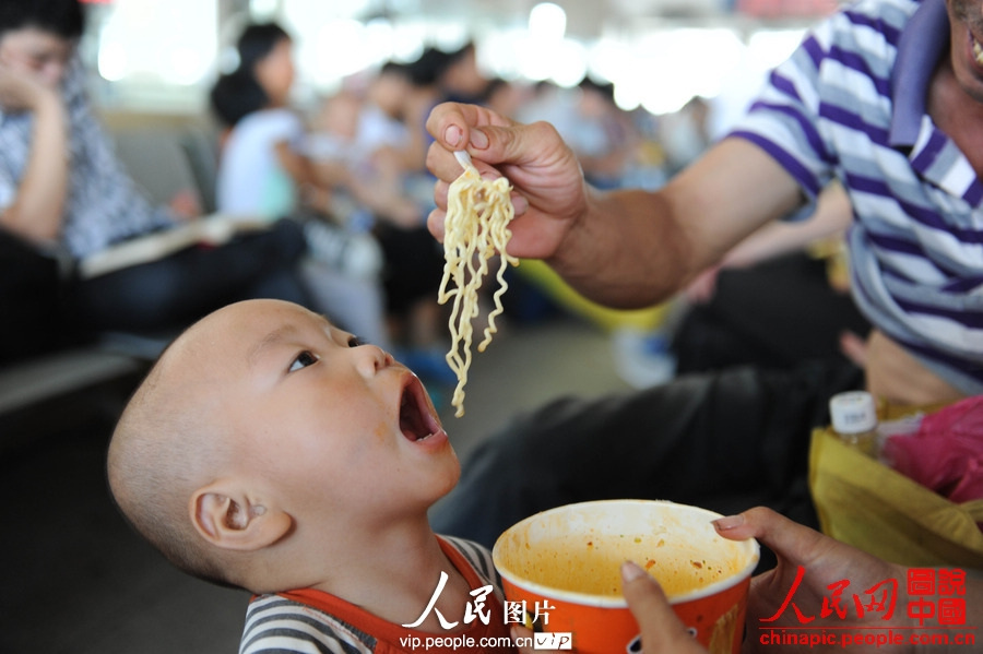 A boy eats noodles in the waiting room of Fuyang Railway Station, east China's Anhui province, July 2, 2013. (photo/vip.people.com.cn)