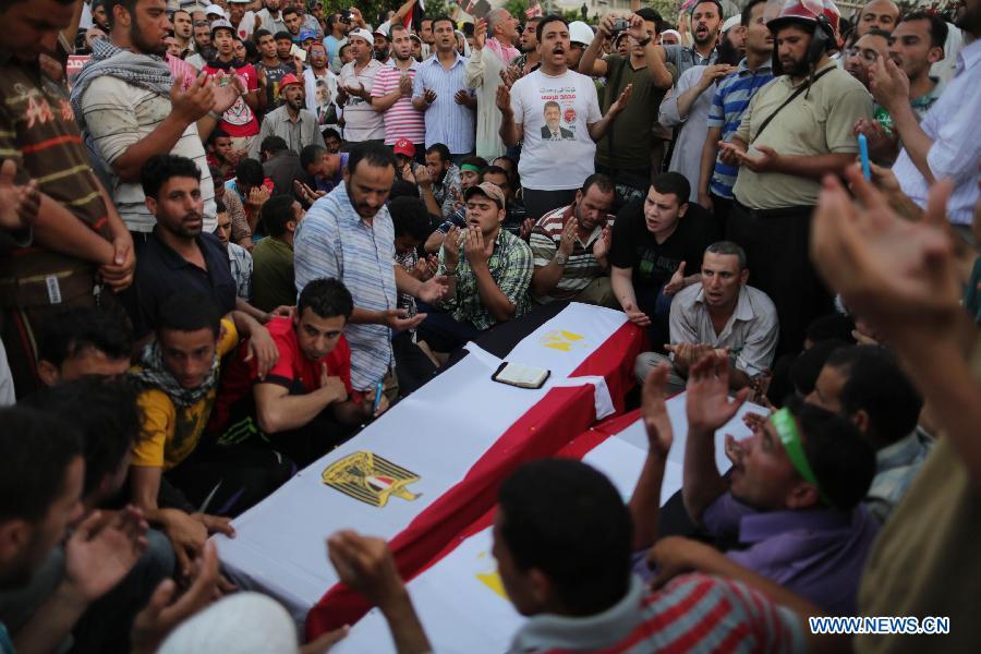 Supporters of ousted Egyptian President Mohamed Morsi sit around the coffins of people killed a day before during the clashes outside the Republican Guard headquarter, in Nasr City, Cairo, Egypt, July 6, 2013. (Xinhua/Wissam Nassar)