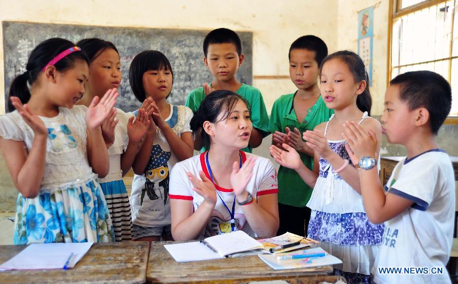 A volunteer sings an English song for left-behind children at Maolong Primary School of Wangdun Township in Duchang County, east China's Jiangxi Province, July 11, 2013. Twenty-four student volunteers of the Wuchang Branch of Huazhong University of Science and Technology came to the primary school to carry out 20-day education support activities for about 200 left-behind children in the summer vacation. (Xinhua/Hu Guolin)