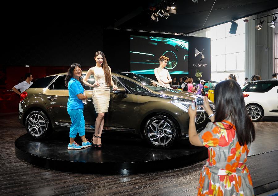 Visitors take photos with a model presenting a vehicle at the 10th China Changchun International Automobile Expo in Changchun, capital of northeast China's Jilin Province, July 12, 2013. The ten-day expo kicked off here on Friday. (Xinhua/Xu Chang)