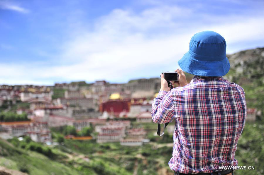 A visitor takes pictures of the Gaden Monastery in Dagze County, southwest China's Tibet Autonomous Region, July 12, 2013. The Gaden Monastery, the first monastery of the Geluk school of Tibetan Buddhism, was set up in 1409. It was listed as one of the first batch of national key cultural relics protection units in 1961. (Xinhua/Liu Kun)